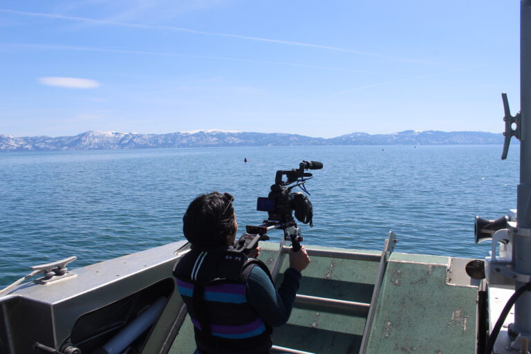 Back side of Vanesa while she is recording the Lake Tahoe, in the background, the mountains.