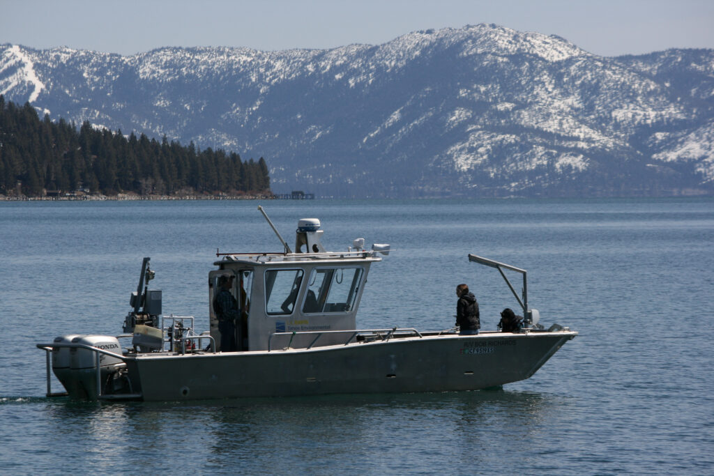 UC Davis research boat in Lake Tahoe. Snowy mountains in the background. Four people, including Vanesa, are in the boat.