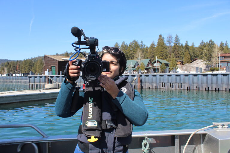 Vanesa in front of the camera, while holding herself a camera in front of her face, at Lake Tahoe.